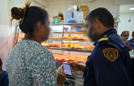 An immigration officer reviewing documents of a foreigner employed at a hotel near Male' marketplace during yesterday's operations. -- Photo: Fayaz Moosa / Mihaaru News