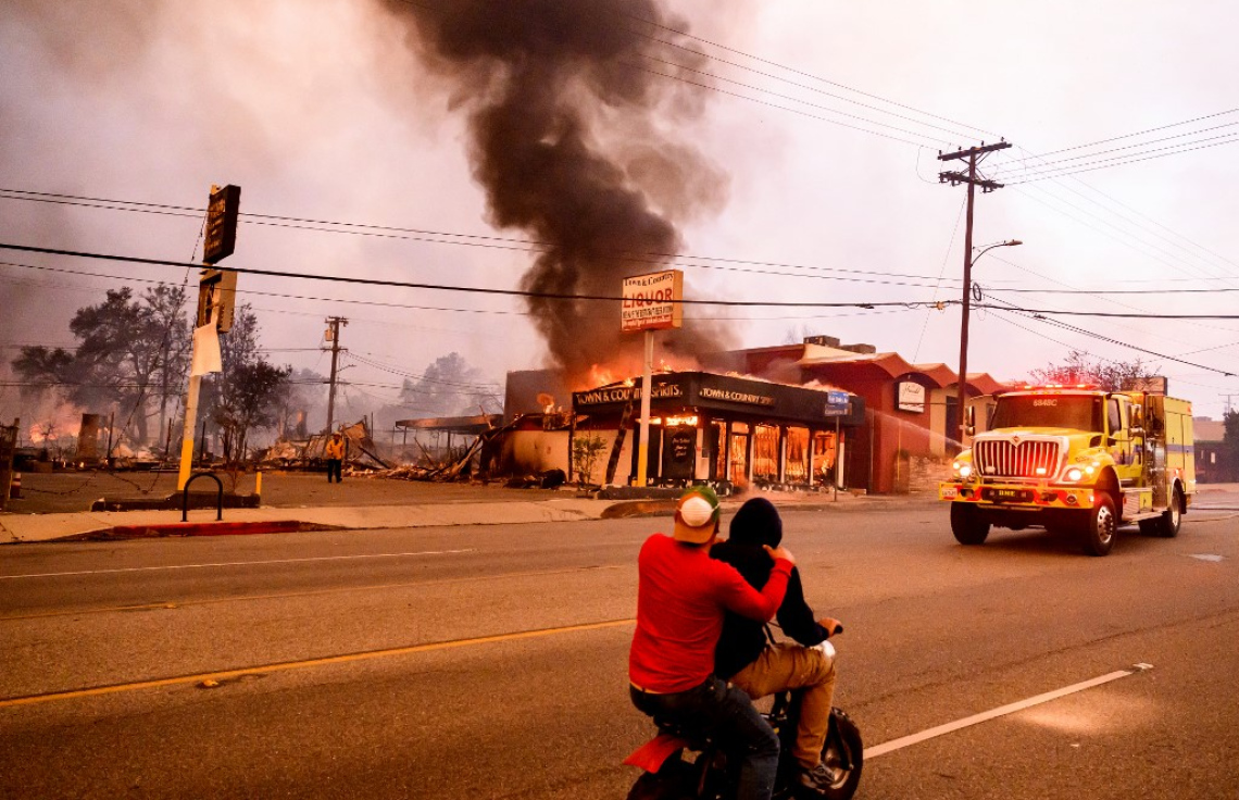 ކެލިފޯނިއާ: ޖެނުއަރީ 8، 2025- އެމެރިކާގެ ކެލިފޯނިއާގެ ލޮސް އެންޖެލިސްގެ އަލްޓަޑެނާ ސަރަހައްދުގައި ހުރި  ފިހާރައެއްގައި ރޯވެ އަނދަމުން ދާއިރު ބަޔަކު އެ ސަރަހައްދުން ދުއްވާފައި ދަނީ. ގަދަ ވަޔާ އެކު އަލިފާން ދަނީ އެކި ހިސާބުތަކަށް ފެތުރެމުން. -- ފޮޓޯ: އޭއެފްޕީ