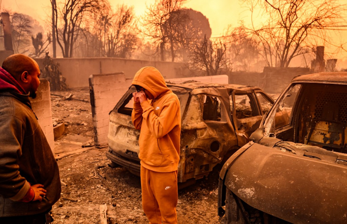 ޖެނުއަރީ 8، 2025- ކެލިފޯނިއާގެ ލޮސް އެންޖެލިސް ކައުންޓީގެ އަލްޓަޑެނާ ސަރަހައްދުގައި އަނދާފައިވާ ގެއެއްގެ ކައިރި ބަޔަކު މަޑުކޮށްލައިގެން. އެމެރިކާގެ ދެ ވަނަ އަށް އެންމެ ބޮޑު ސިޓީ ކަމަށްވާ ކެލިފޯނިއާގެ ވަށައިގެން އަލިފާން ރޯވެ އަނދަމުން ދާއިރު 1،000 އަށް ވުރެ ގިނަ އިމާރާތް އަނދައި، އެތައް ހާސް ބަޔަކު ގެދޮރު ދޫކޮށް ދާން ވަނީ މަޖުބޫރުވެފައި. -- ފޮޓޯ: އޭއެފްޕީ