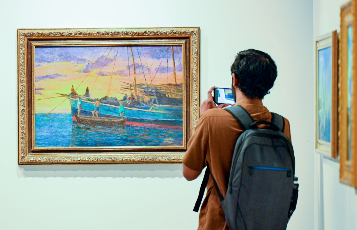 ރާއްޖޭގެ އެހާރާއި މިހާރުގެ ދިރިއުޅުން ދައްކުވައިދޭ ކުރެހުންތަކާ އެކު، އާޓް ގެލެރީގައި މިހާރު ކުރިއަށް ގެންދާ މަނާގޭ އަބްދުﷲ ފާއިޒުގެ ކުރެހުމުގެ މައުރަޒަށް ޒިޔާރަތްކުރި ޒުވާނަކު ކުރެހުމުގެ ފޮޓޯއެއް ނަގަނީ: މި މަހުގެ 16 އިގެ ނިޔަލަށް މި މައުރަޒު ކުރިއަށް ގެންދާނެ.---ފޮޓޯ: ނިޝާން އަލީ| މިހާރު