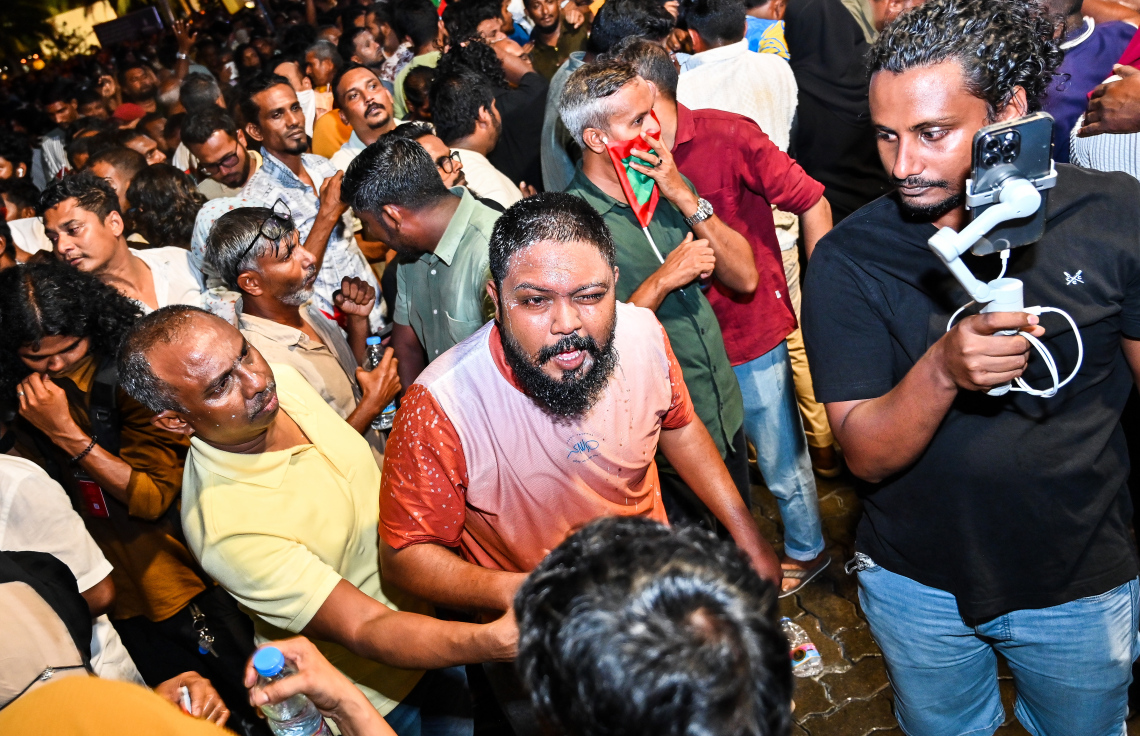 އިދިކޮޅު އެމްޑީޕީގެ ބޮޑު އެއްވުމުގެ ބައިވެރިން ފުލުހުންގެ އެންގުމާ ހިލާފަށް މަޖީދީ މަގުން ދާން މަސައްކަތް ކުރުމުން، އެ މީހުން ފަހަތަށް ޖައްސަން ފުލުހުން ޕެޕާސްޕްރޭ ޖެހުމާ ގުޅިގެން ލޮލަށް ފެން އަޅަނީ.---ފޮޓޯ: ފަޔާޒު މޫސާ| މިހާރު