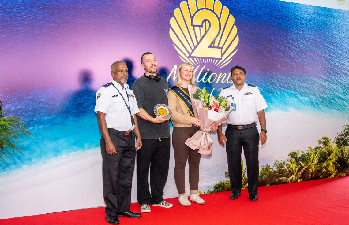 ރާއްޖެ އަށް ޒިޔާރަތްކުރި ދެ މިލިއަން ވަނަ ޓޫރިސްޓުގެ ޝަރަފު ހޯދި އިނގިރޭސި ވިލާތުގެ ބެތަނީ ސާރާ ކާސްވެލްއާ އެކު، ކަސްޓަމްގެ ދެ އޮފިސަރަކު ފޮޓޯއެއް ނަގަނީ.---ފޮޓޯ: ނިޝާން އަލީ| މިހާރު