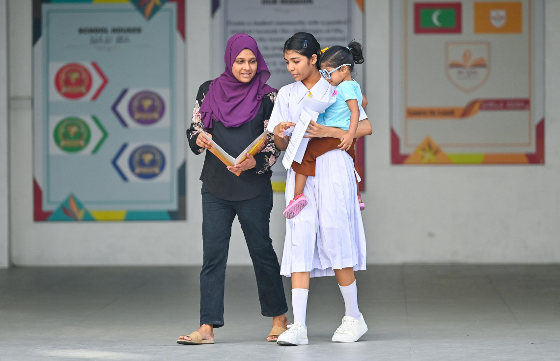 ދަރިވަރަކު ރިޕޯޓު ފޮތް ހިފައިގެން ބެލެނިވެރިއަކާ އެކު ދަނީ.-- ފޮޓޯ: ފަޔާޒް މޫސާ / މިހާރު